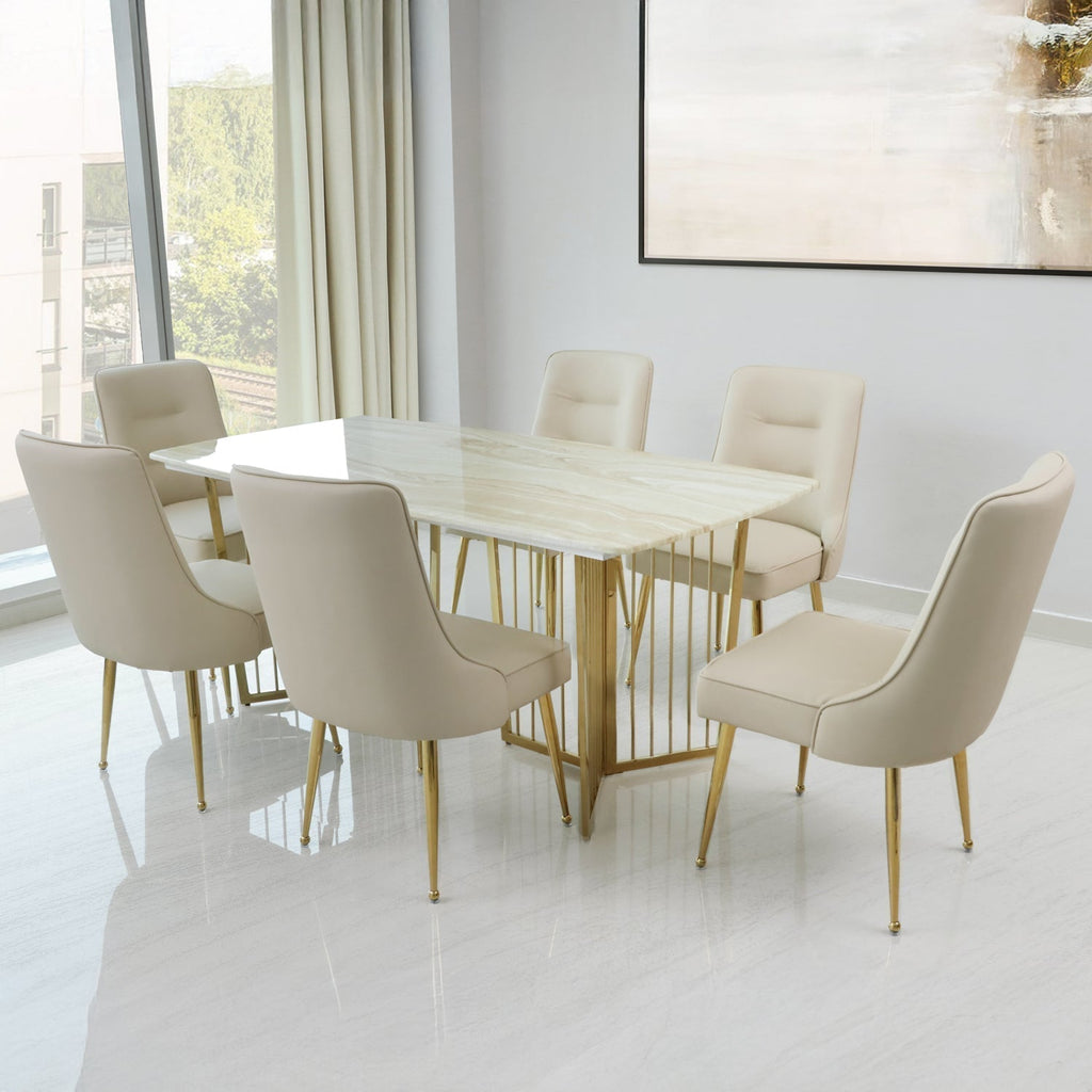 Elegant marble dining table set with a polished marble-top table and six beige cushioned chairs featuring gold metal legs, placed in a bright modern dining room with large windows and minimalist decor.